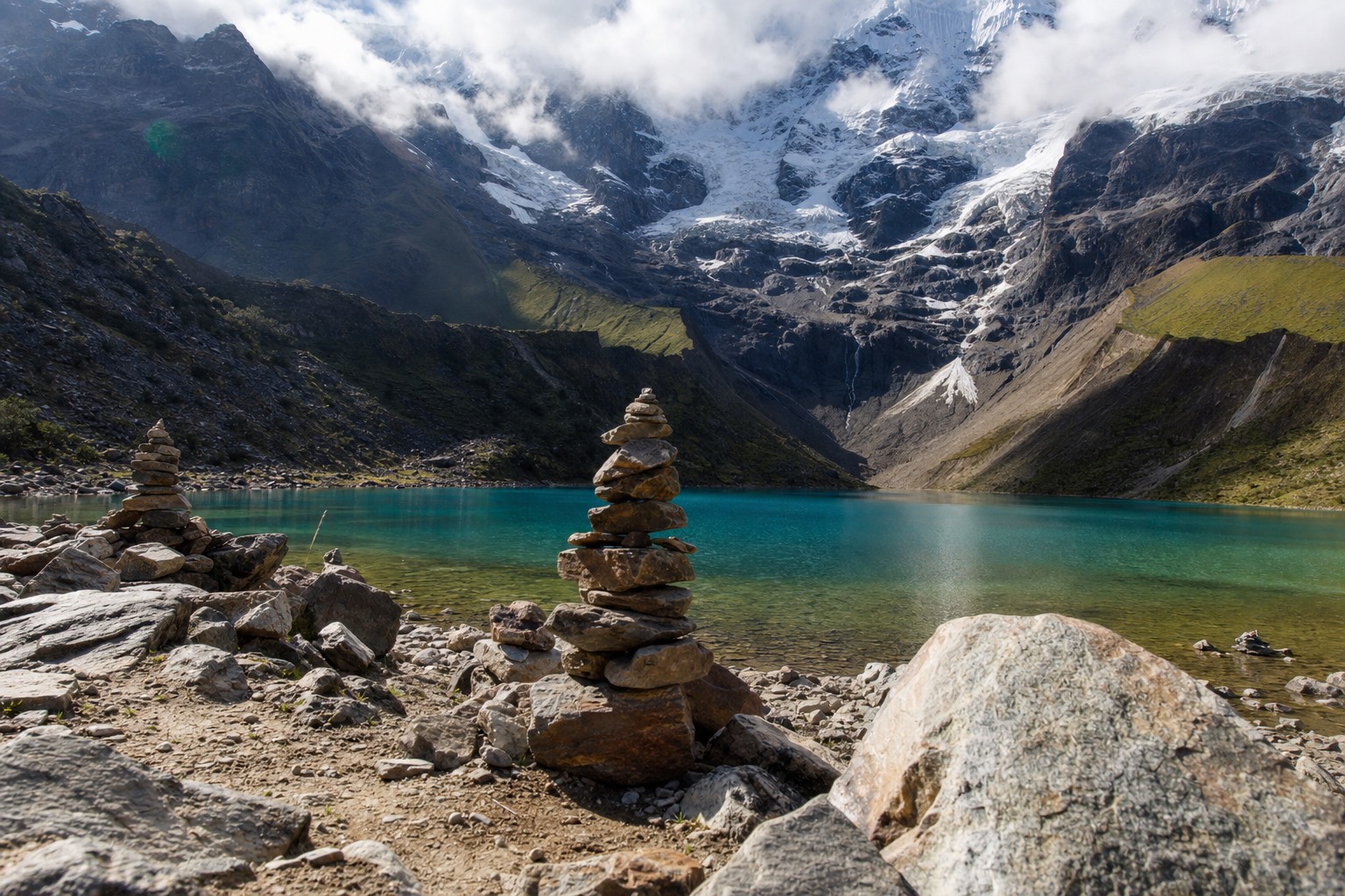 Stacked stone apachetas on the shore of Humantay Lake with the glacier behind them