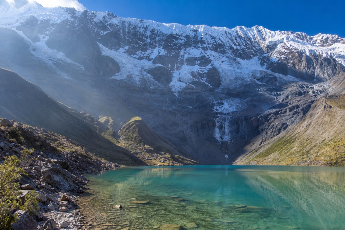 Early morning hikers arriving at Humantay Lake while the glacier stands clear above still turquoise water