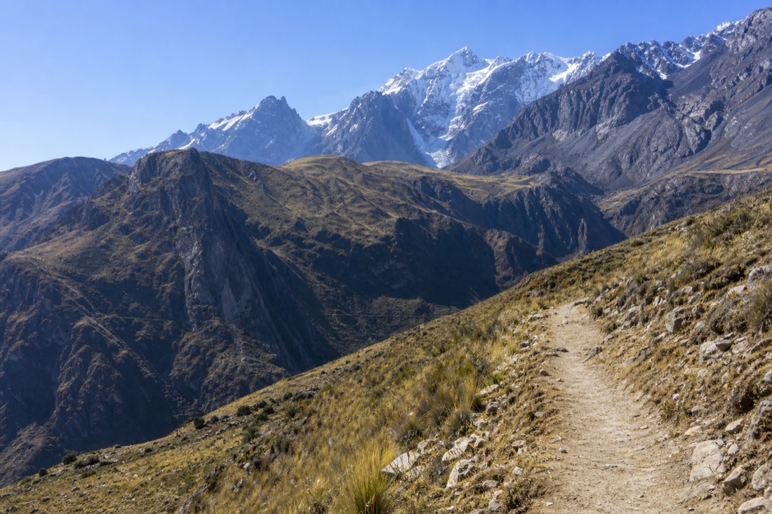 Firm dusty trail above Soraypampa in late dry season with fresh snow on the peaks and thin high-altitude grass, no people