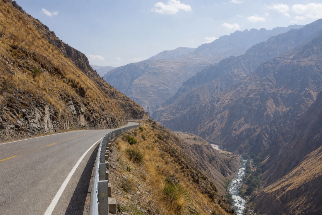 Paved highway winding through the warm Apurimac canyon near Limatambo with dry slopes and a river far below, no vehicles