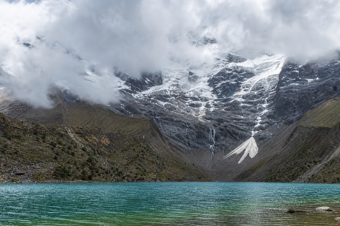 Grey afternoon cloud rolling across the glacier above Humantay Lake with wind rippling the turquoise water, no people