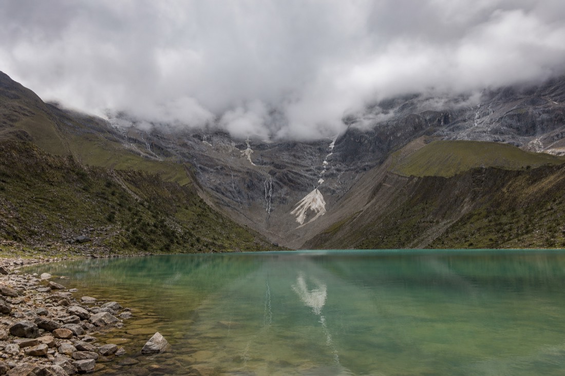 Humantay Lake under heavy overcast, its water a muted jade green with cloud hiding the glacier