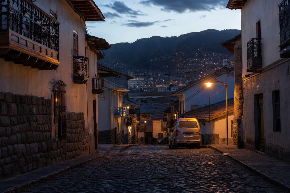 Empty cobbled street in Cusco's historic centre before dawn, colonial balconies and a single van waiting under a street lamp