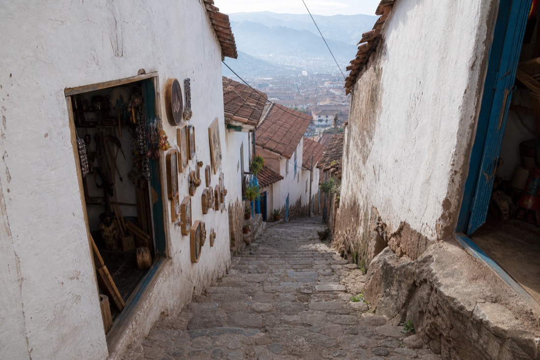 Steep whitewashed lane in San Blas, Cusco, with stone steps and artisan workshop doorways