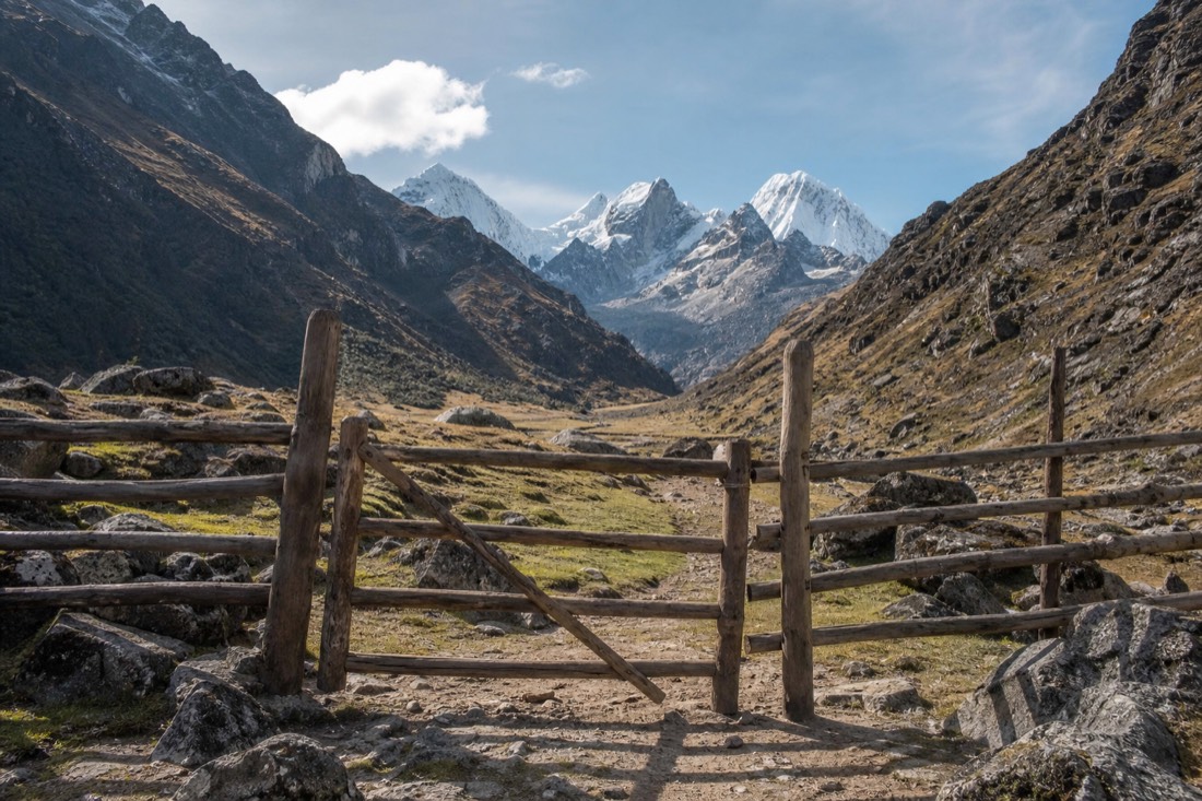 Rustic timber control gate at the Soraypampa trail entrance with the rocky valley and snow peaks beyond, no people and no signage